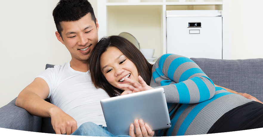 Smiling pregnant couple reclining on a couch and looking at a tablet