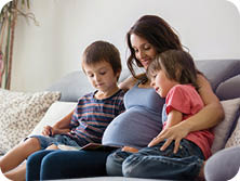 Young pregnant woman, reading a book at home to her two boys, eating fruits, hugging and laughing
