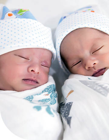 Newborn twins laying next to each other wearing hats and wrapped in blankets