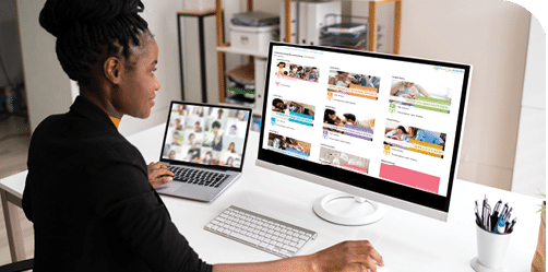 Woman sitting at a desk with a large screen and laptop to one side