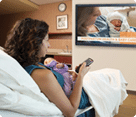Woman sitting in hospital bed watching InJoy's postpartum video program on a TV on the wall
