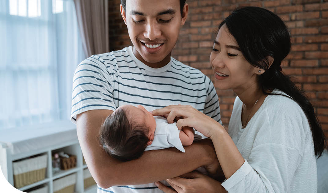 Smiling father holding newborn baby while mother caresses baby's chin